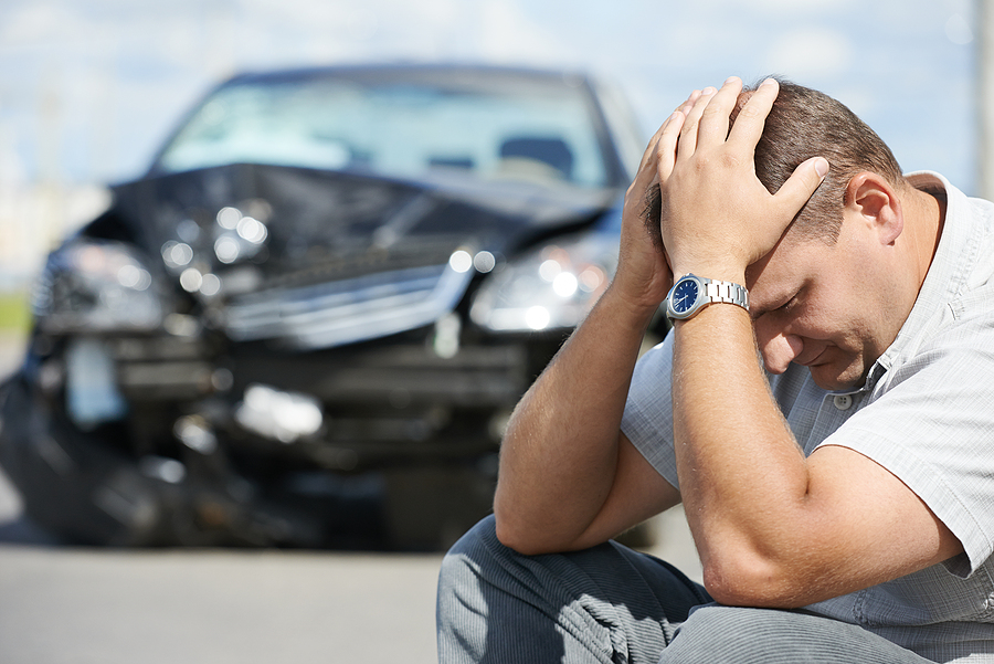 Upset man sits on the curb in front of his damaged car