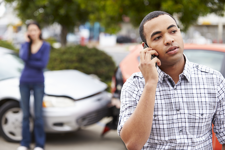 Man talking on the phone after a car accident with the other driver and the damaged cars in the background