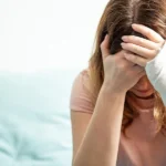 Woman with a cast on her arm holding her head and crying because she is suffering from mental health issues after a car accident