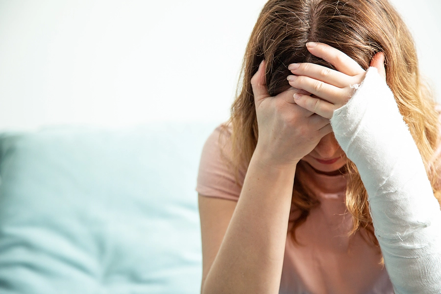Woman with a cast on her arm holding her head and crying because she is suffering from mental health issues after a car accident