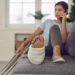 Woman undergoing rehabilitation after a car accident cause her ankle injury sits on the couch talking on the phone