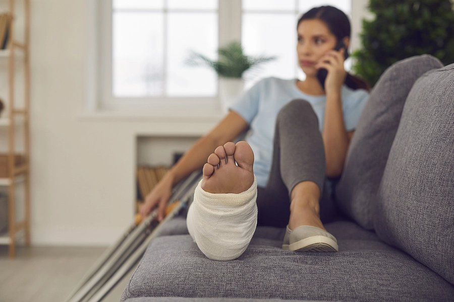 Woman undergoing rehabilitation after a car accident cause her ankle injury sits on the couch talking on the phone