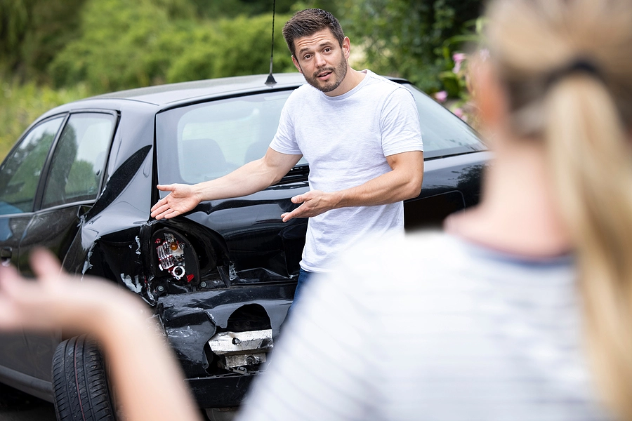 Man and woman arguing over who is at fault for a rear-end accident standing next to their damaged cars