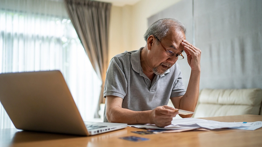 older asian man filing florida bankruptcy petition, looking stressed as he reviews paperwork at home