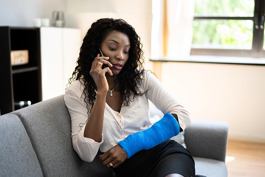 Woman with a cast on her arm sitting on her couch talking to her Florida personal injury lawyer about her case on the phone