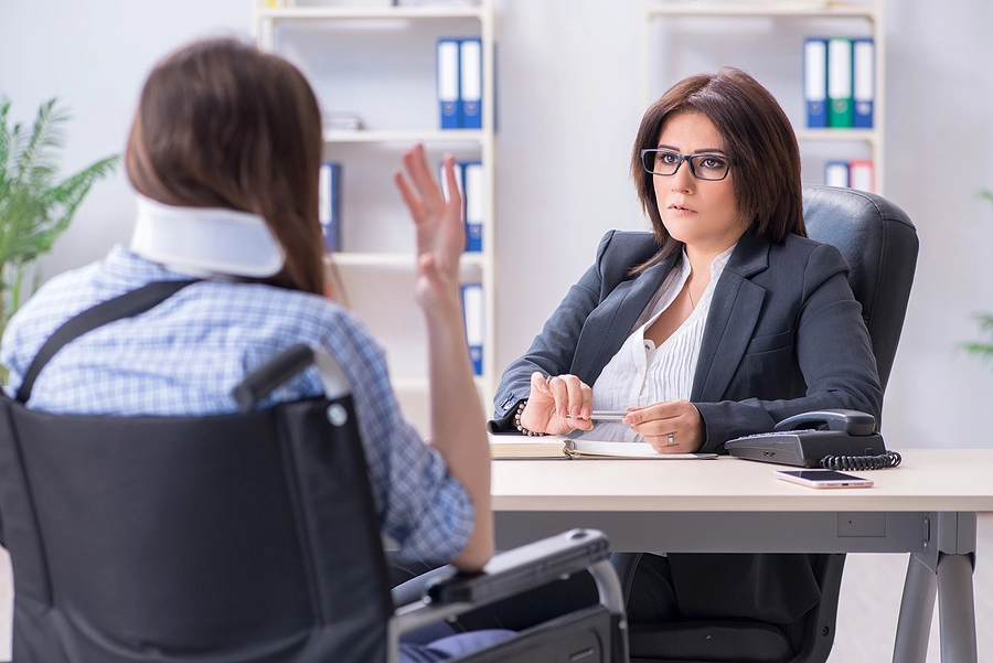 man with a wheelchair and neck brace discusses his case with a hollywood personal injury lawyer in her office