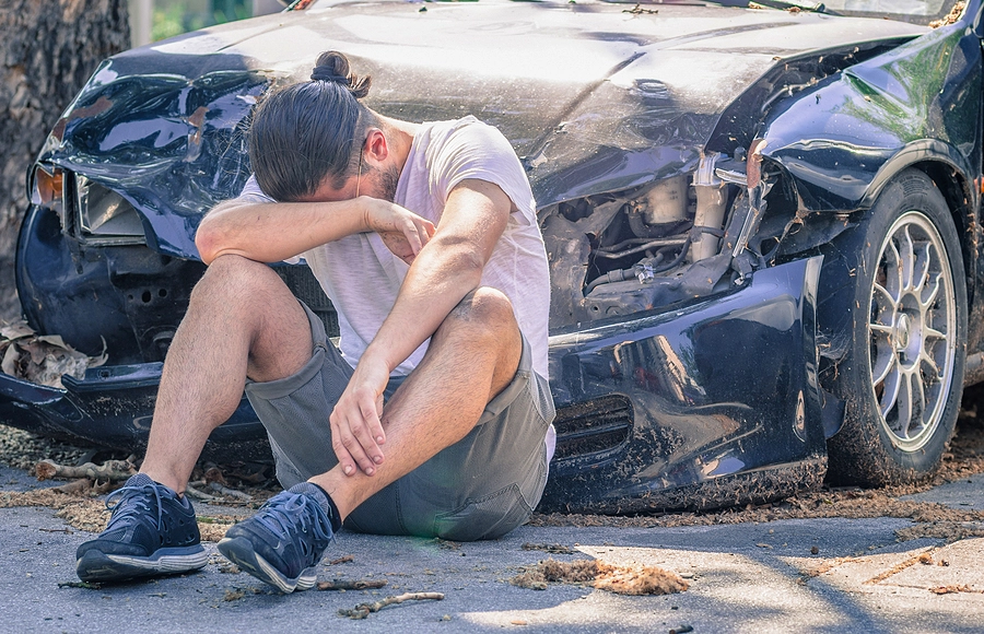 Crying man sits on the ground in front of his damaged vehicle after a Miami car accident