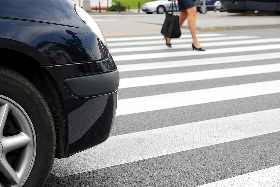 Pedestrian crossing a street in front of a car at a crosswalk