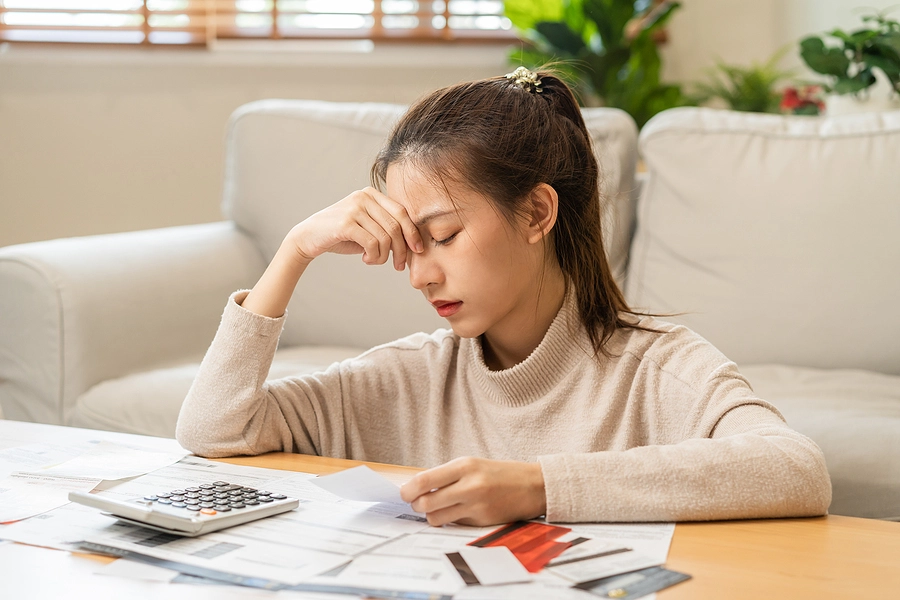 young woman with bills and calculator looking stressed trying to decide when to file for bankruptcy