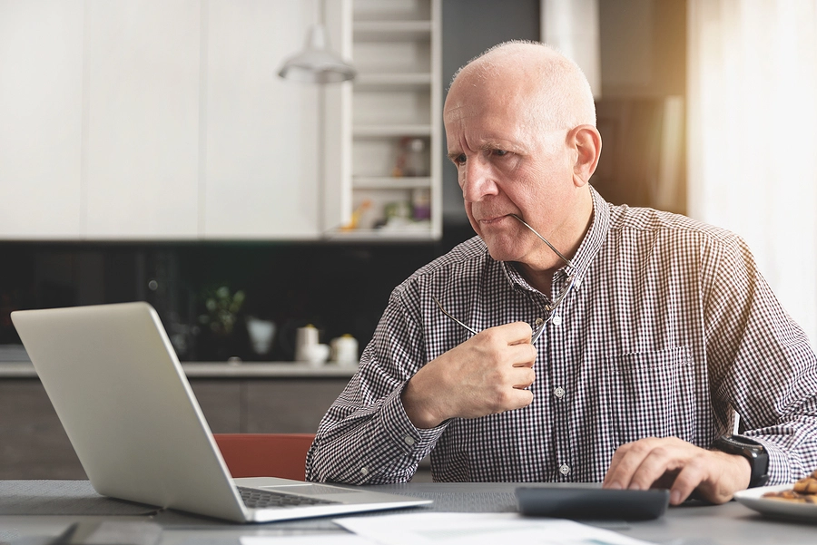 older male veteran with glasses reading about va pensions and benefits on his laptop