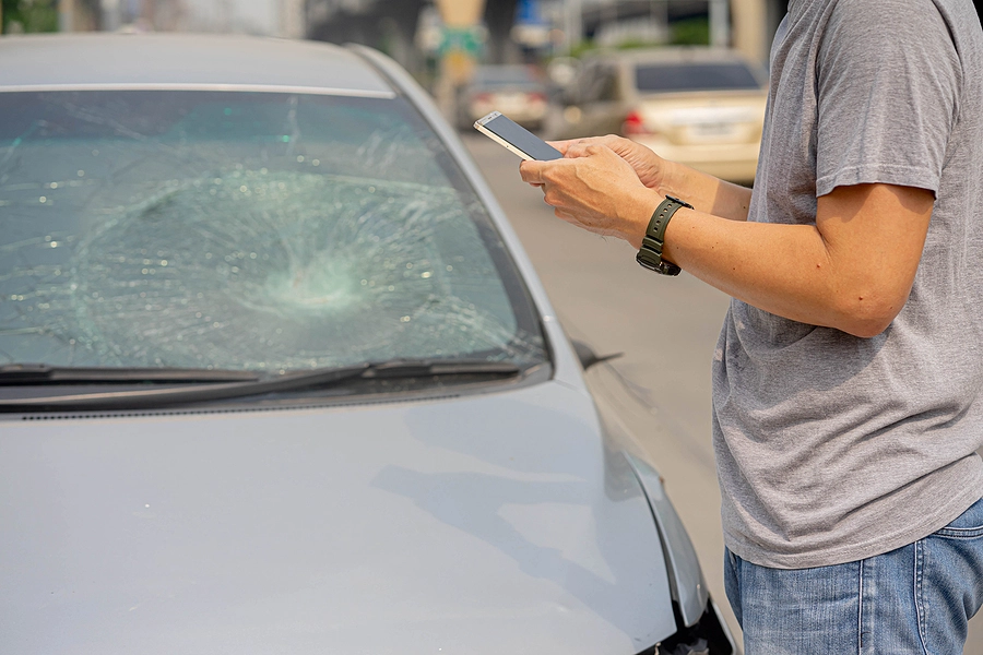 driver who was just in a crash stands outside of his car and dials a boynton beach car accident lawyer