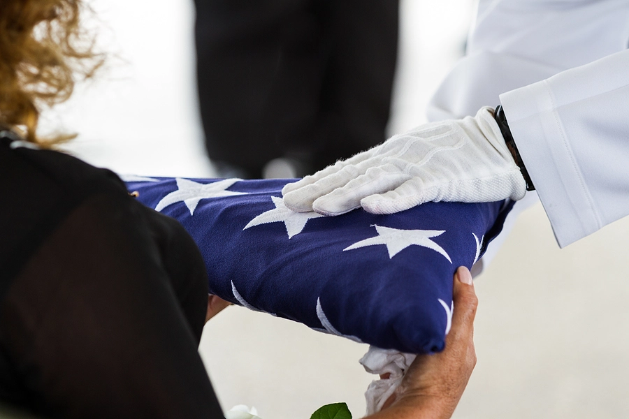 survivors and dependents of a deceased veteran who are potentially eligible for va benefits receiving a folded flag at a funeral