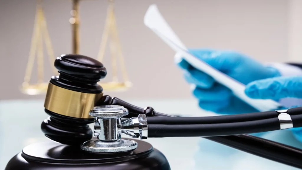 Close-up of a gavel, stethoscope, and a hand holding a document wearing blue gloves.