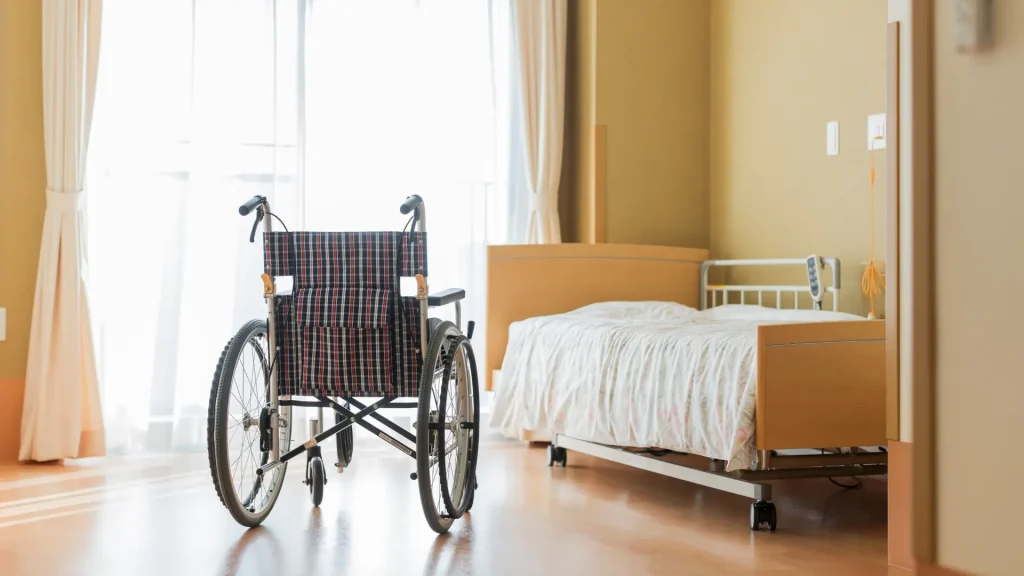 Empty wheelchair beside a hospital bed in a room with natural light