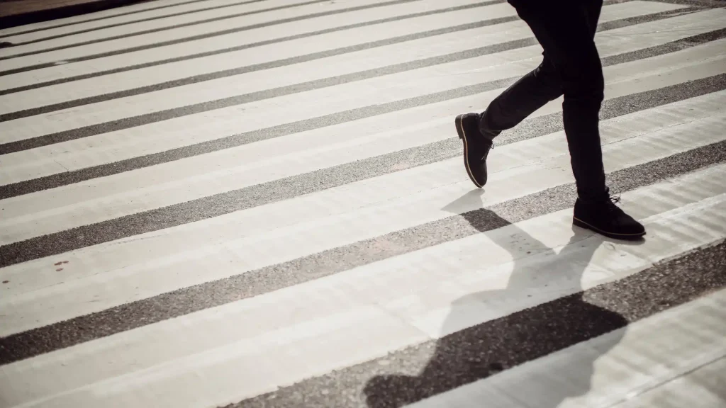 Person walking across a crosswalk, casting a shadow on the ground
