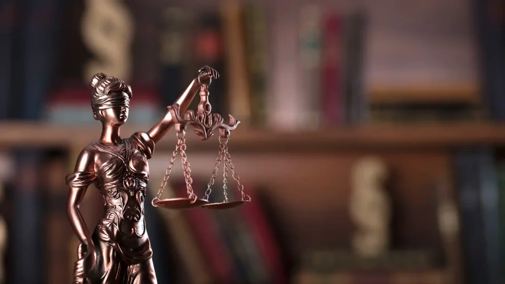 Statue of Lady Justice with scales, against a blurred background of law books.