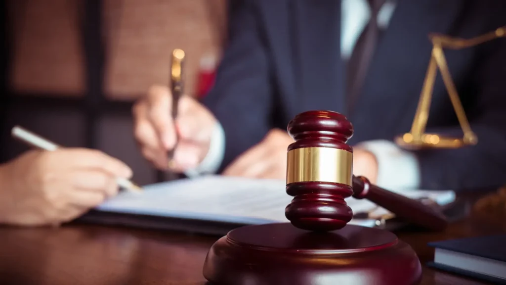 Close-up of a gavel and legal documents with two people discussing in the background.