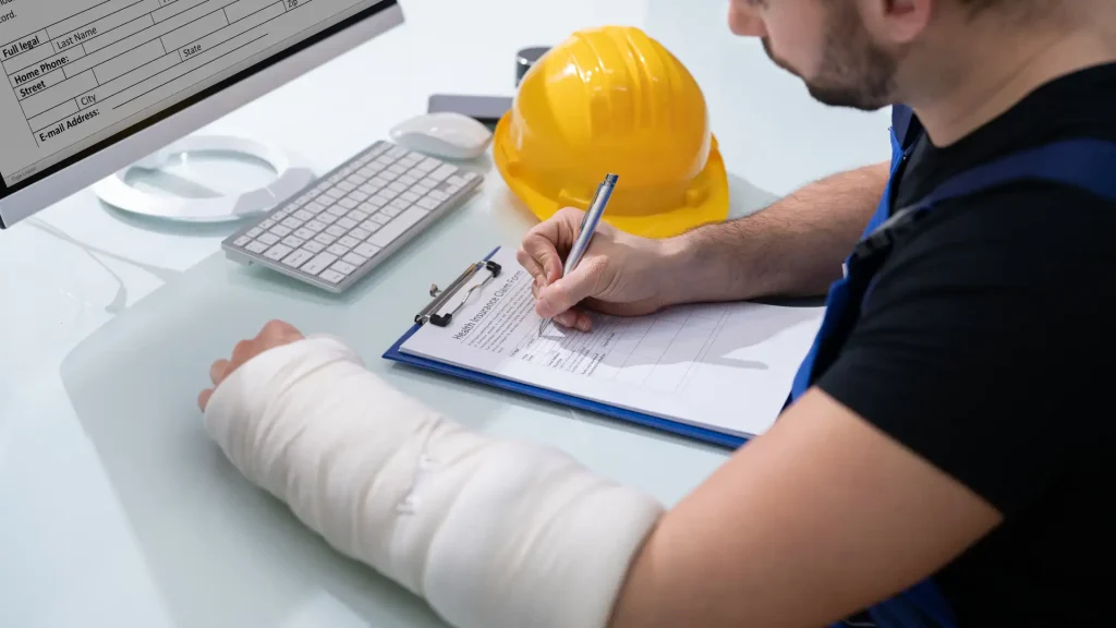 Injured worker with a bandaged arm filling out a report at a desk.