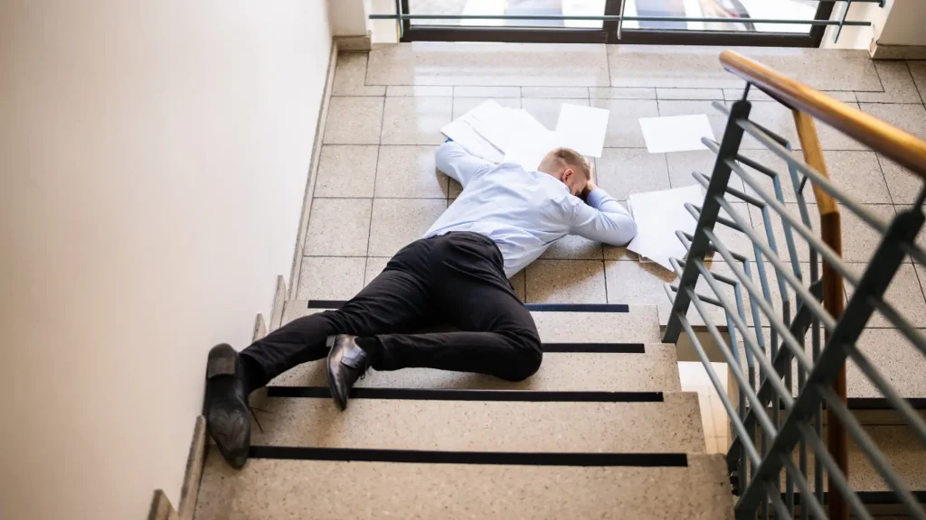 Person lying on the stairs after a fall, with papers scattered around.