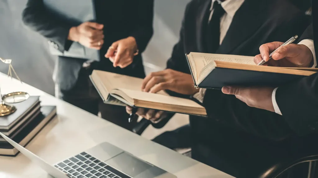 Lawyers reviewing legal books and documents during a discussion, with a laptop in front.