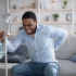 Young man with a spinal cord injury struggles to stand up from his couch with the aid of a crutch