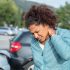 Woman grabs her neck while clearly in pain in front of a car accident scene