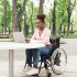 Young woman in wheelchair works on her laptop at a table outside